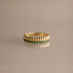 The Ribbed Emerald Stack Ring is a gold band with a sculpted ribbed texture and a row of small green emeralds at the center, perfect for everyday ring stacks and shown against a plain background.