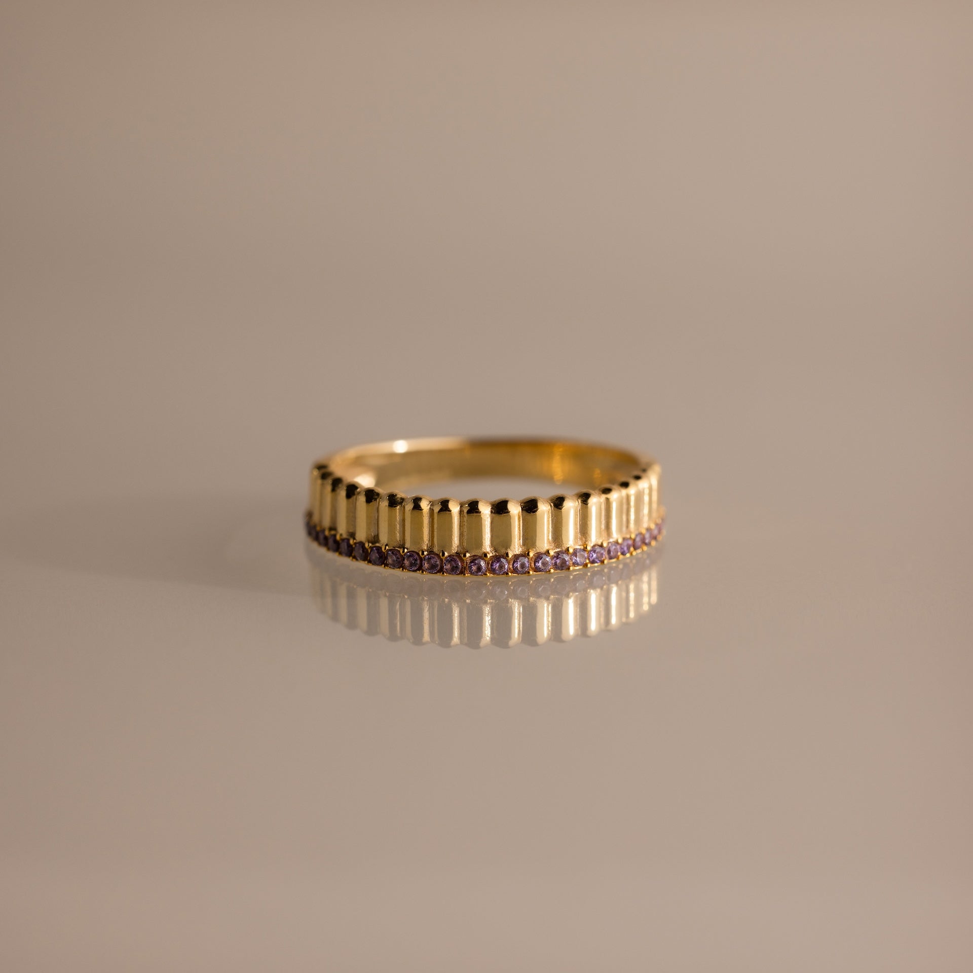 Ribbed Alexandrite Stack Ring with vertical ridges and a row of small purple alexandrite stones, shown on a neutral reflective surface.