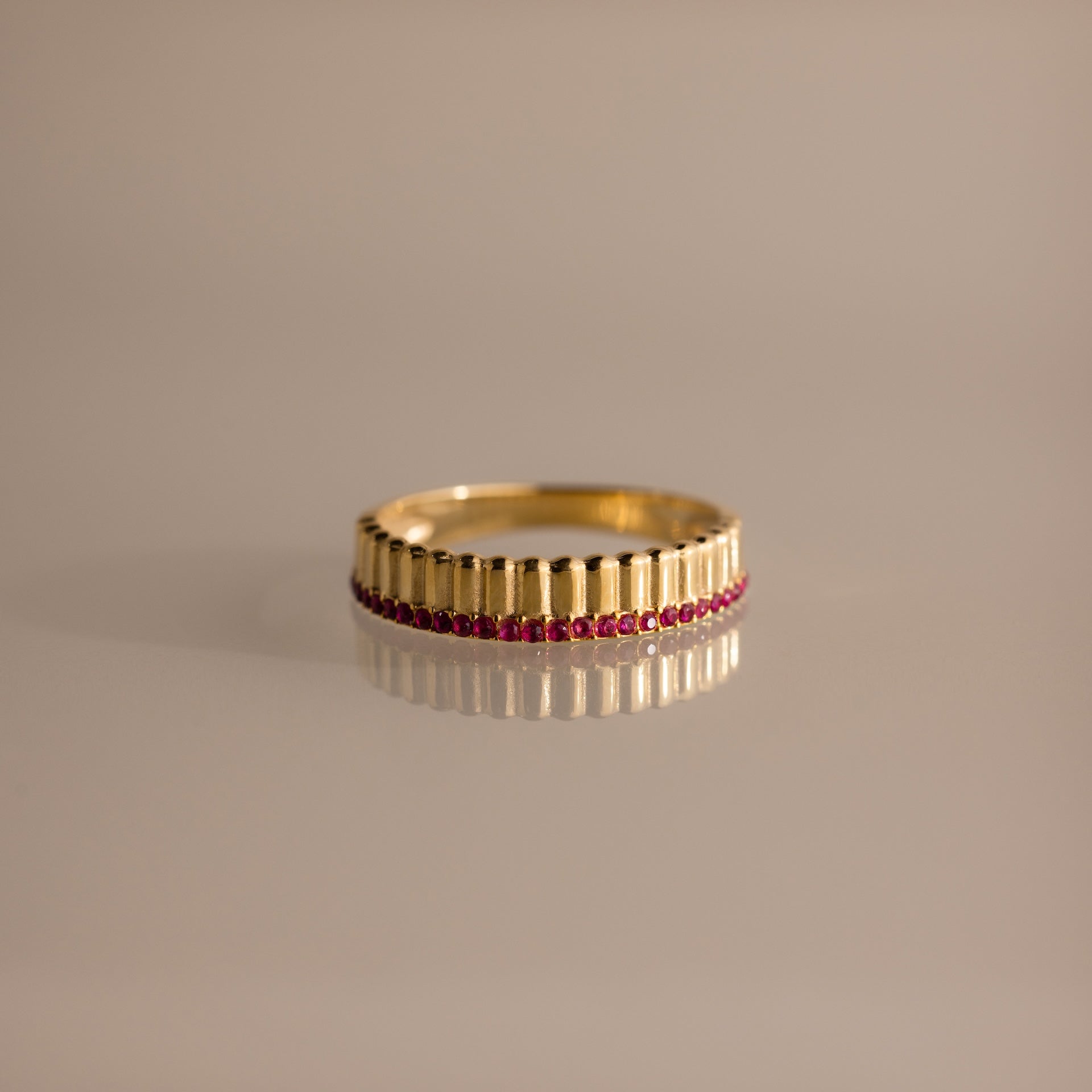The Ribbed Ruby Stack Ring features vertical ridges and a row of small red rubies near the base, making it a unique addition to your ring stack. Shown on a neutral background.