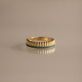 The Ribbed Blue Zircon Stack Ring features a gold band with small blue stones in a row, perfect for stacking and shown on a reflective surface.