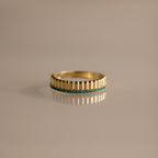 The Ribbed Blue Zircon Stack Ring features a gold band with small blue stones in a row, perfect for stacking and shown on a reflective surface.