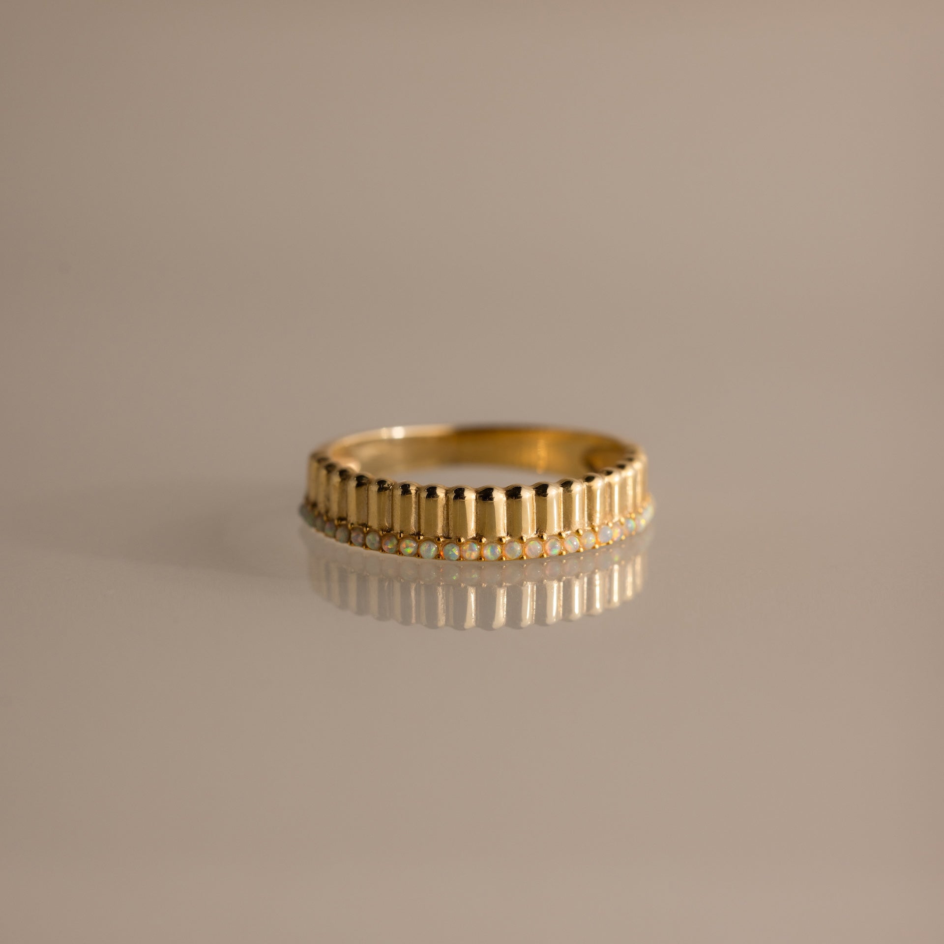 The Ribbed Opal Stack Ring features a beaded edge and small opal stones, beautifully displayed on a reflective surface—ideal for adding texture to your ring stack.