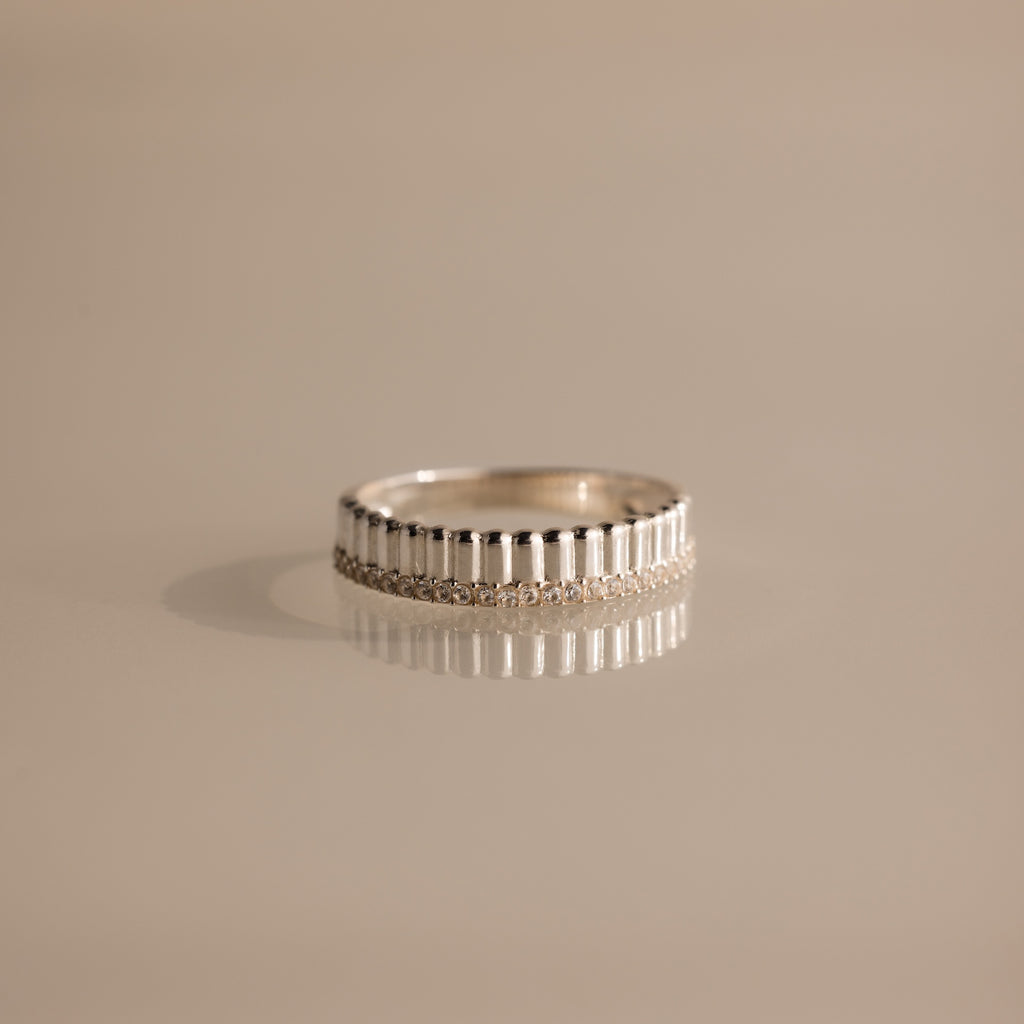 A Ribbed Diamond Stack Ring featuring a textured pattern is displayed on a smooth, light beige surface.