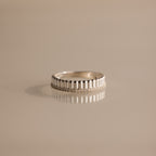 A Ribbed Diamond Stack Ring featuring a textured pattern is displayed on a smooth, light beige surface.