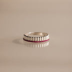 Ribbed Ruby Stack Ring with a row of small red gemstones set in the center, shown on a beige surface.