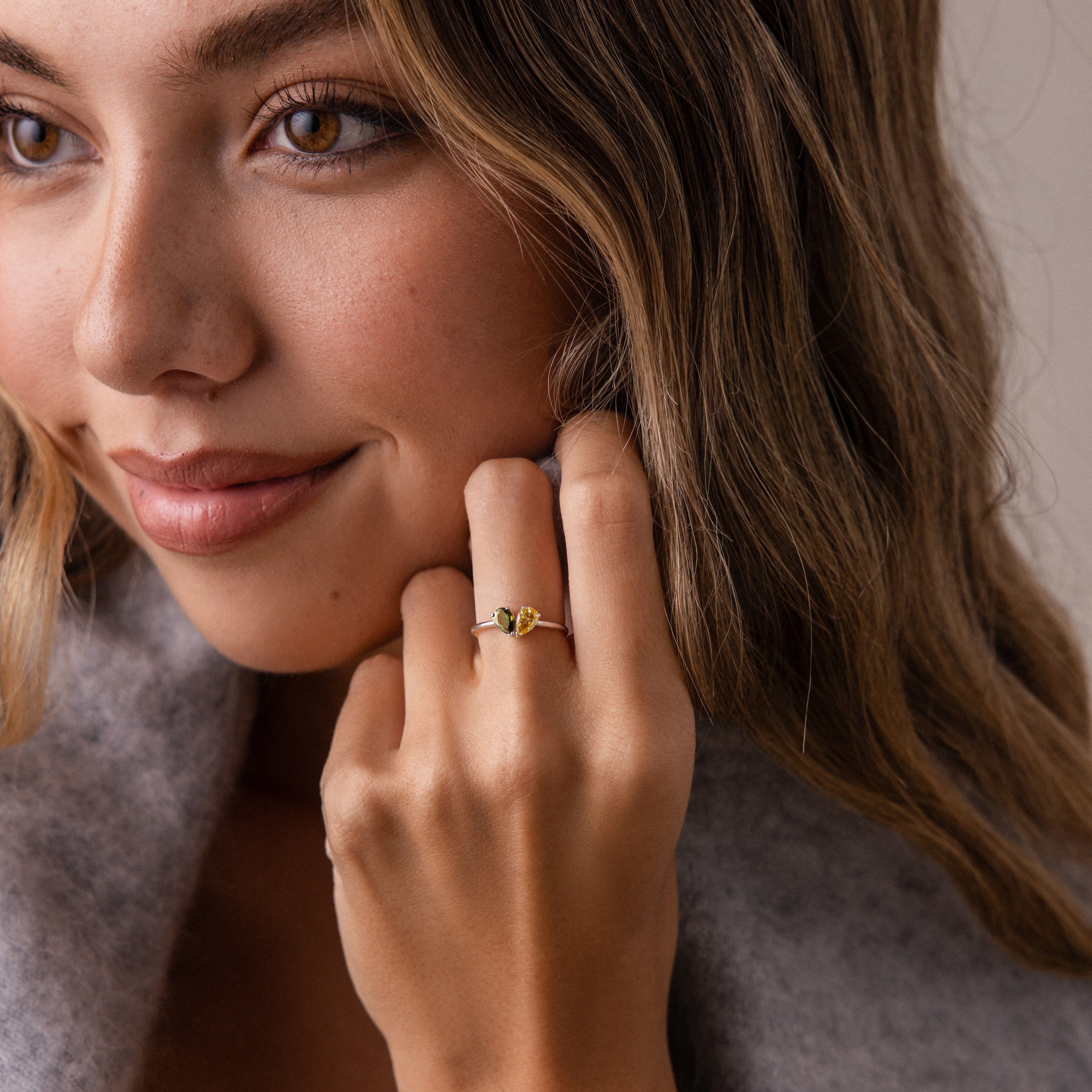 A woman with wavy hair smiles softly, showcasing the Toi et Moi Teardrop Heart Ring in Sterling Silver on her finger.