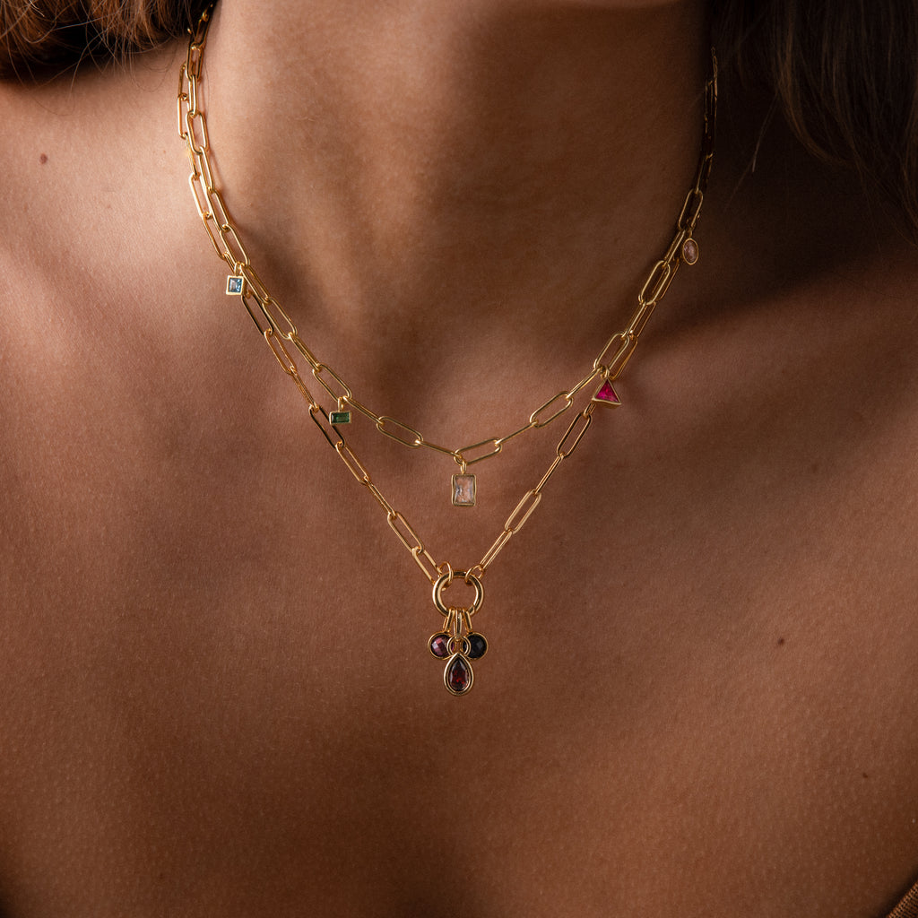 The Mixed Birthstone Charm Necklace in Rose Gold features two gold chains with colorful birthstone charms resting elegantly on a woman’s neck and collarbone.