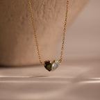 The Toi et Moi Teardrop Heart Necklace in 18K Gold showcases two small heart-shaped stones—one dark, one light—gracefully set against a neutral background.