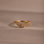 Gold pave curve ring with a round center diamond and shimmering pave set stones along the band, displayed on a soft neutral background.