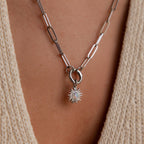 Silver sun charm with an opal center on a paperclip chain necklace, worn over a textured beige top.