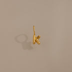 The Bubble Letter Charm in 18K Gold, shaped as a K, makes a stylish personalized pendant or bracelet charm and is showcased on a neutral beige background with a soft shadow.