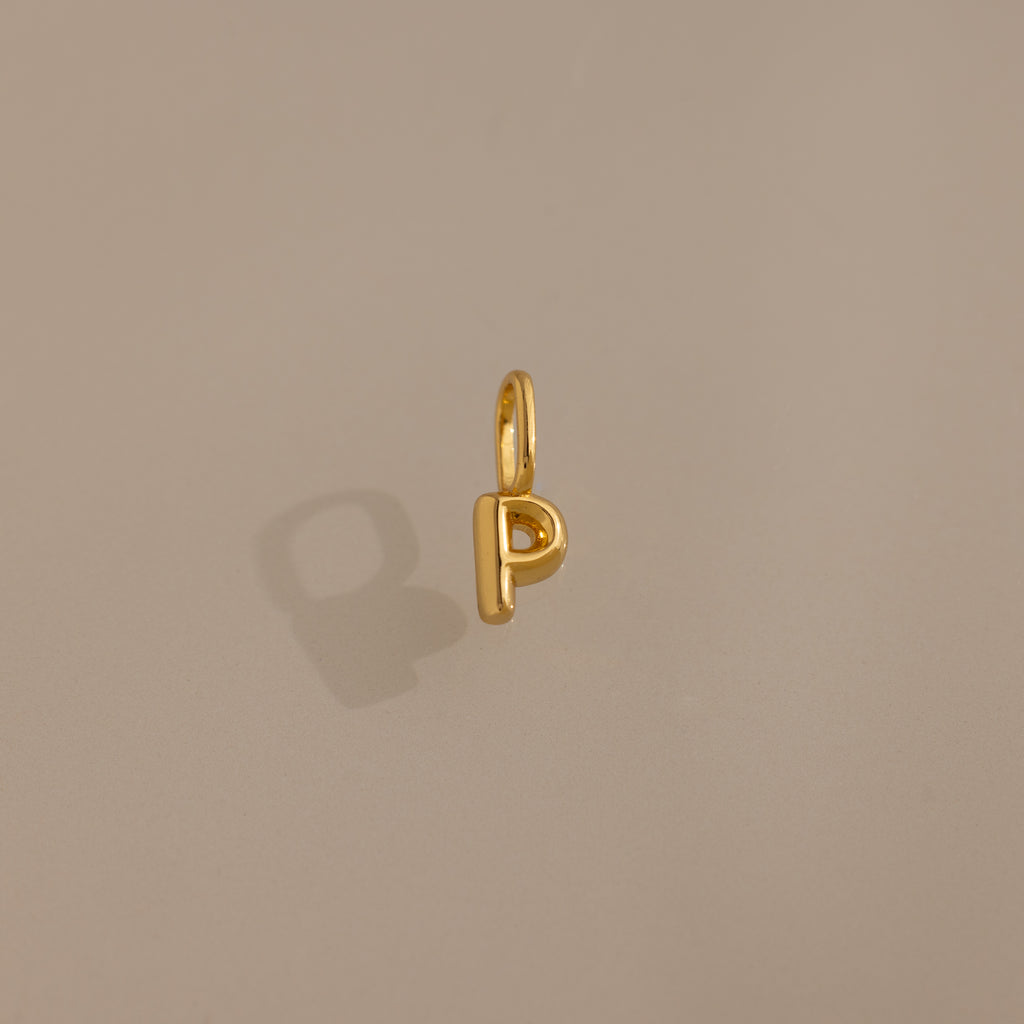 The Bubble Letter Charm in 18K Gold shaped like the letter P rests on a plain beige background, making it an ideal personalized jewelry piece or trendy charm for bracelet lovers.
