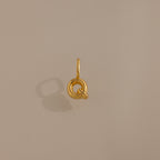 The Bubble Letter Charm in 18K Gold is a circular gold pendant with a small loop, shown on a beige background with a soft shadow—ideal for personalized jewelry or bracelet lovers.