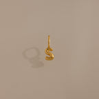 The Bubble Letter Charm in 18K Gold casts a shadow on a plain beige surface, making it a standout accessory—ideal as personalized jewelry or a unique addition to bracelet collections.