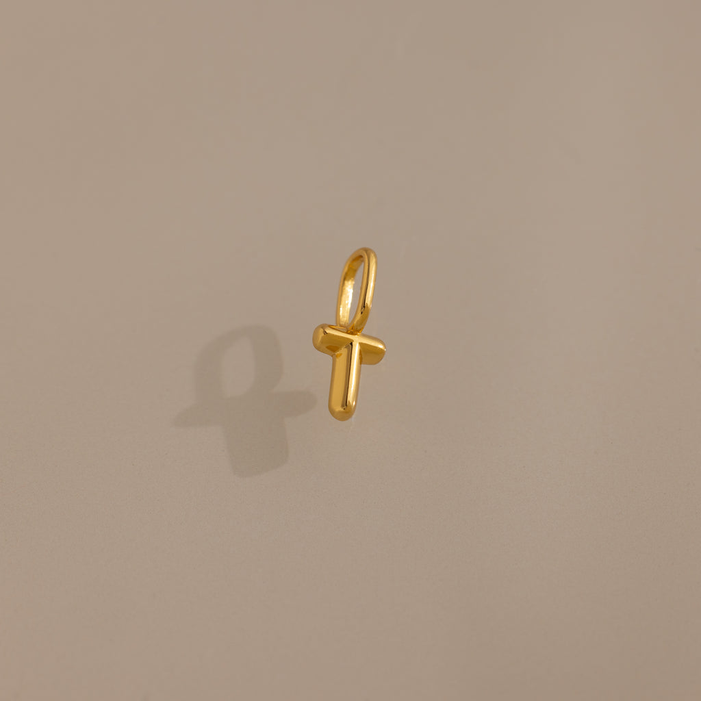 The Bubble Letter Charm in 18K Gold, shaped like the letter T, rests on a beige background—a perfect personalized jewelry piece or stylish charm for bracelet lovers.