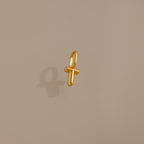 The Bubble Letter Charm in 18K Gold, shaped like the letter T, rests on a beige background—a perfect personalized jewelry piece or stylish charm for bracelet lovers.