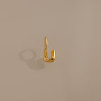 The Bubble Letter Charm in 18K Gold forms a striking U-shape on a beige surface, making it an ideal personalized jewelry piece or charm for bracelet lovers.