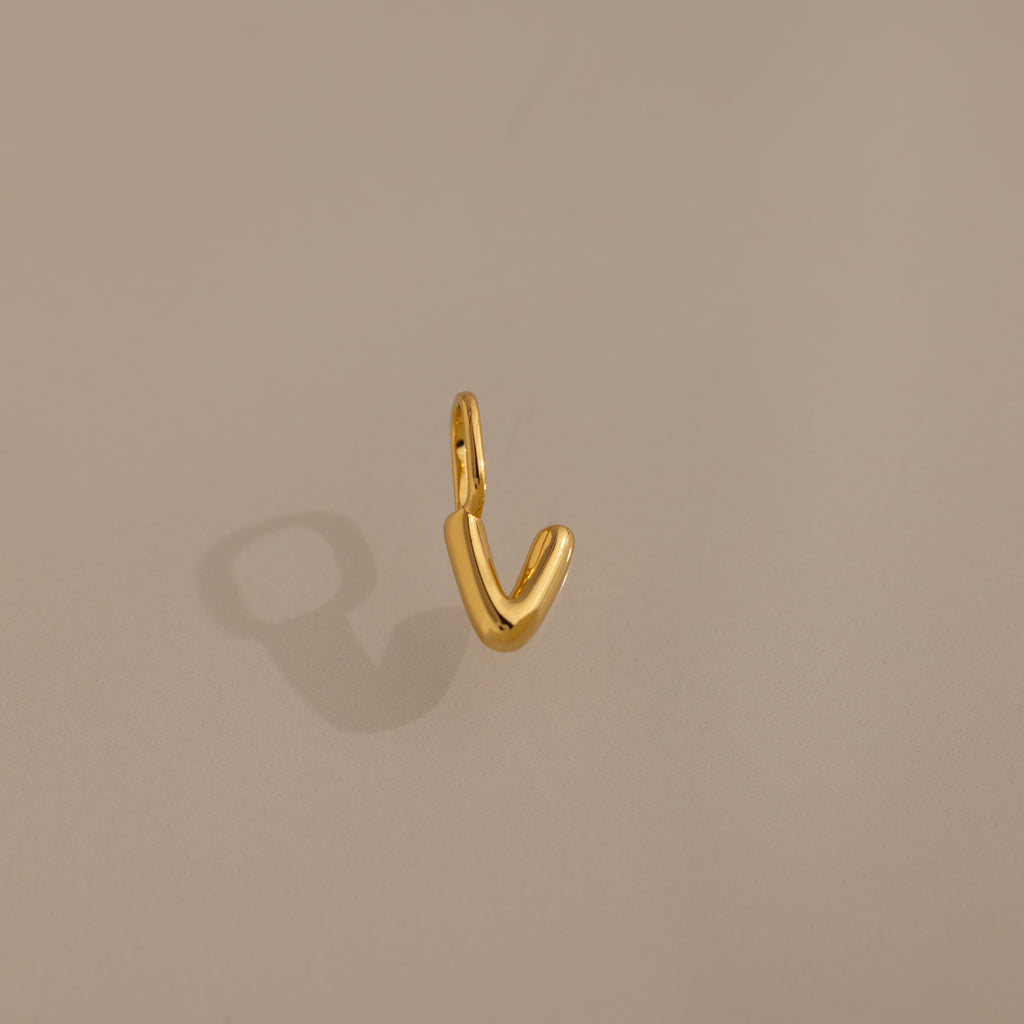 The Bubble Letter Charm in 18K Gold shines with a smooth, V-shaped design on a beige background—ideal as a personalized jewelry accent for bracelet lovers.