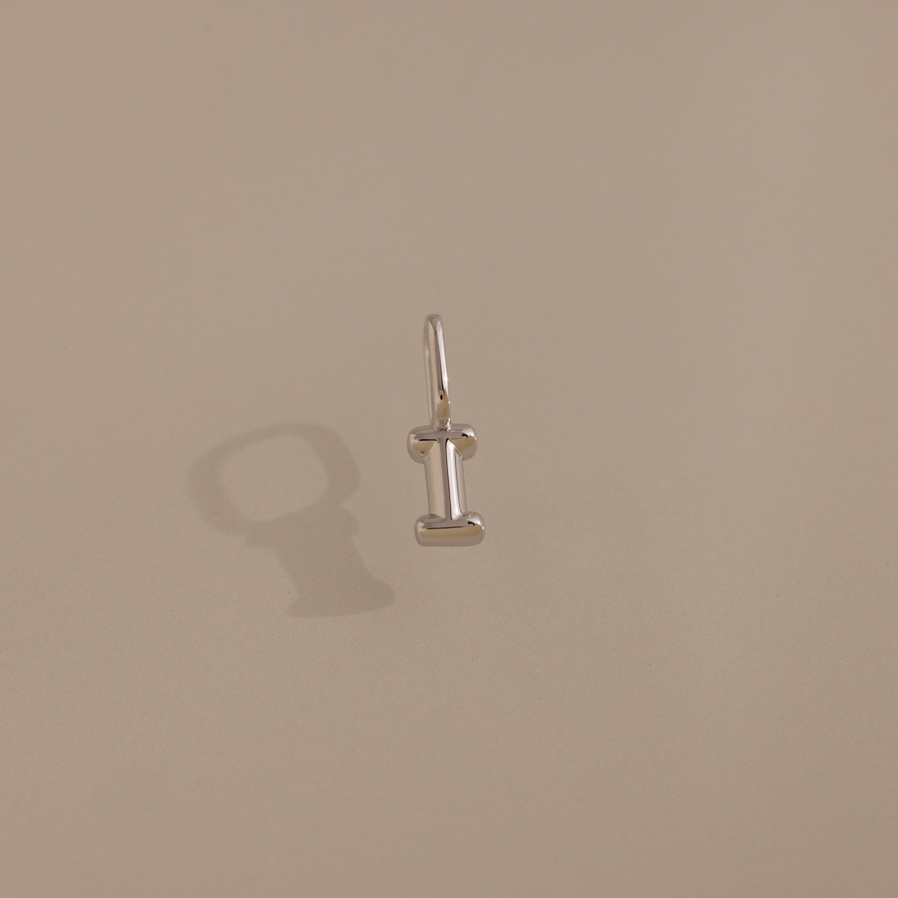 The Bubble Letter Charm in Sterling Silver, shaped like the letter I, is displayed on a beige background—a modern accessory ideal for personalizing your style.