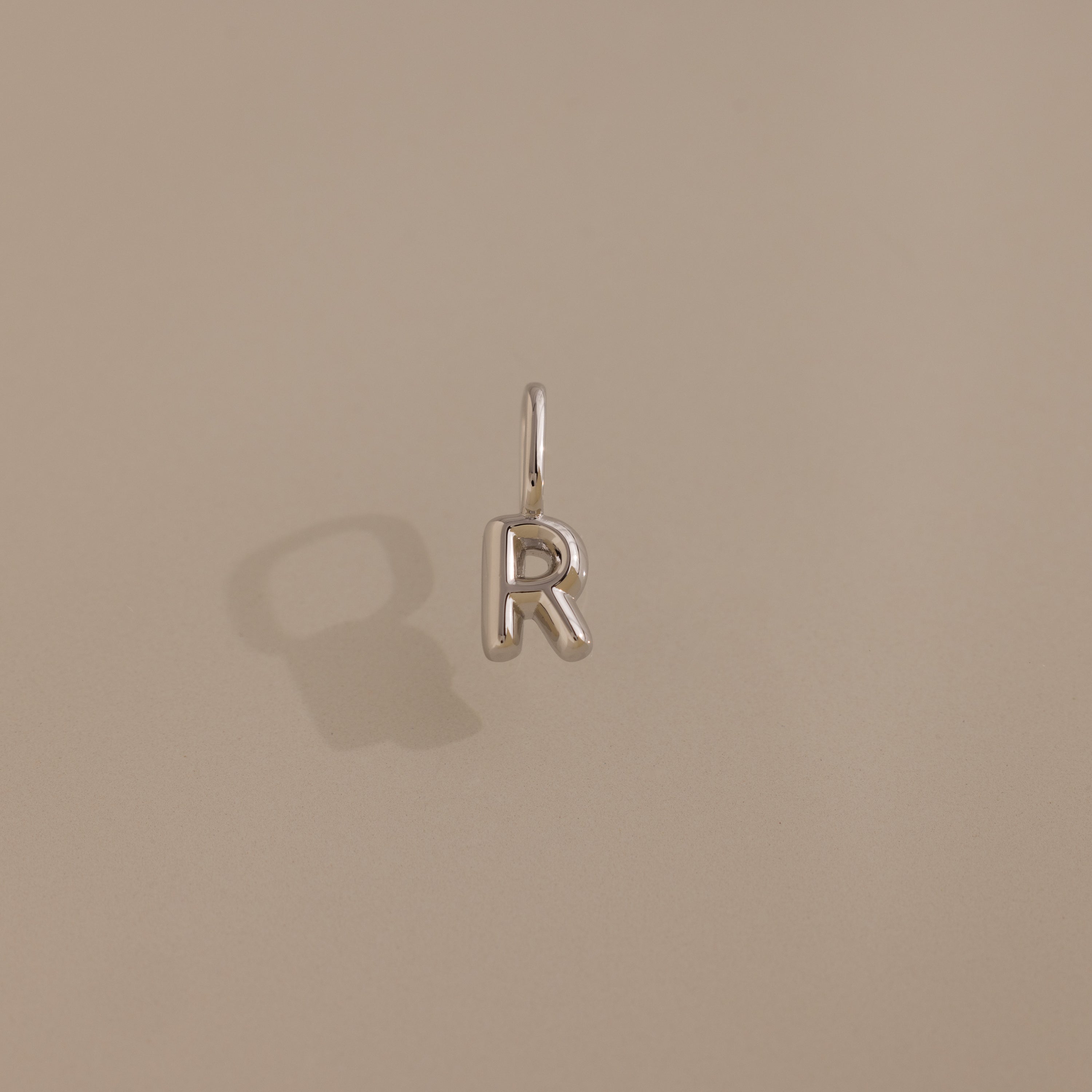Bubble Letter Charm in Sterling Silver, shaped as an "R", displayed on a beige background with a gentle left shadow—an ideal accessory to personalize your jewelry style.