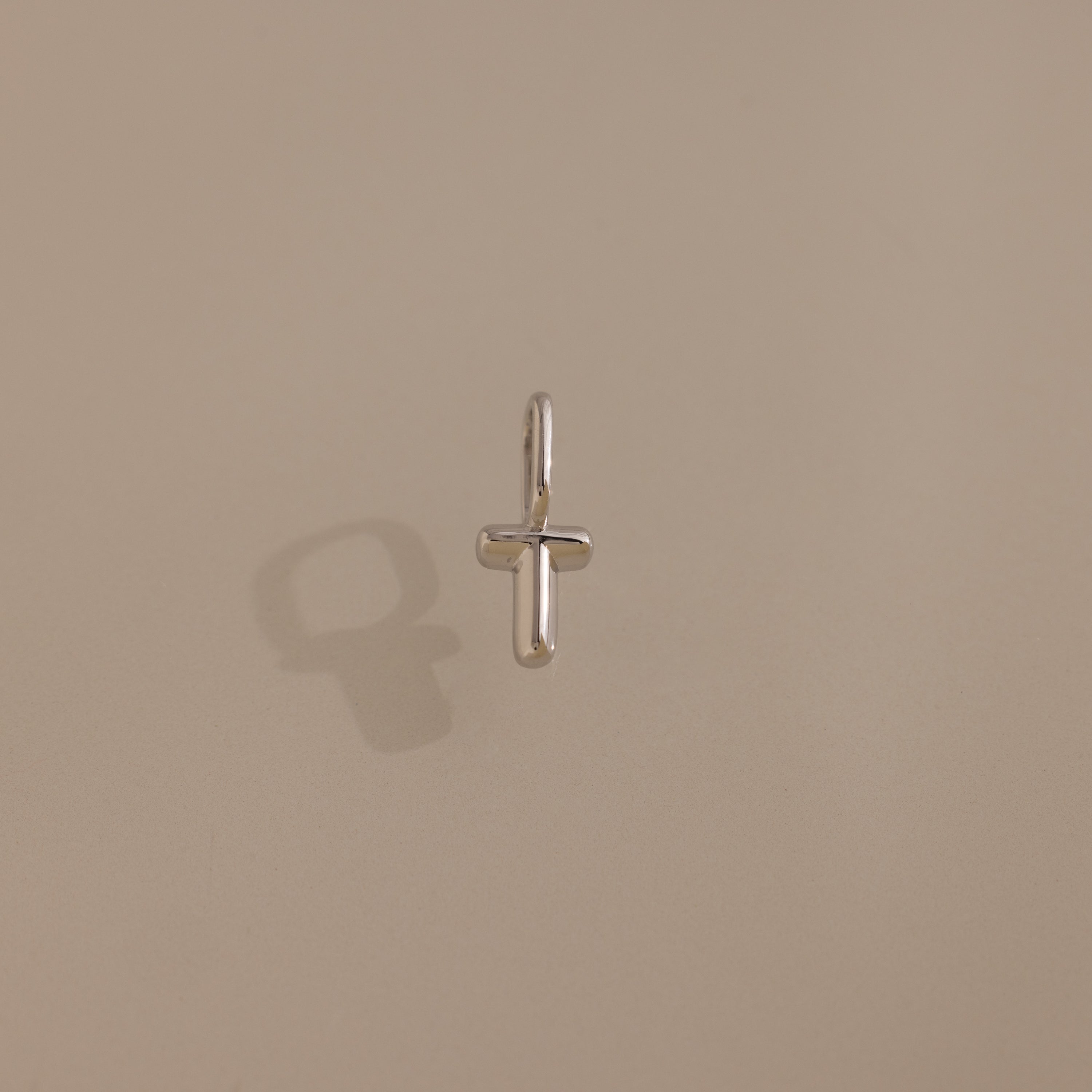 The Bubble Letter Charm in Sterling Silver, attached to a small hoop earring, casts a delicate shadow on a beige surface.