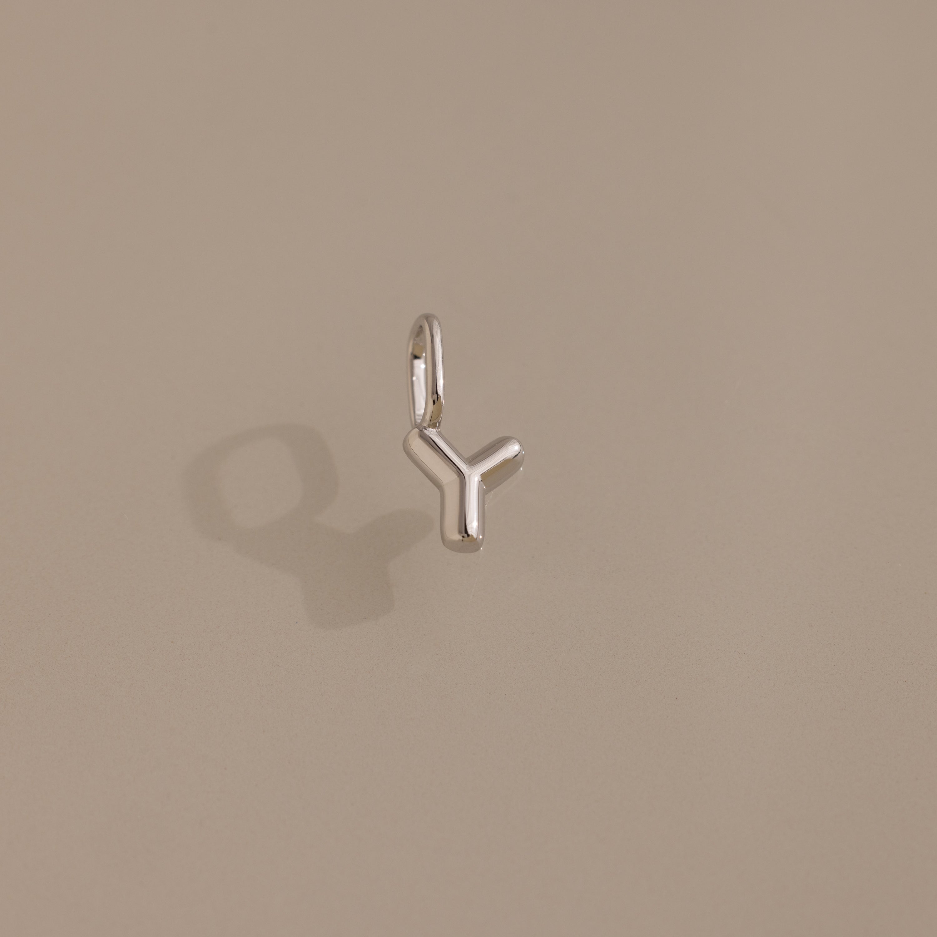 The Bubble Letter Charm in Sterling Silver is a personalized pendant shaped like the letter Y, shown here shining against a neutral beige background.
