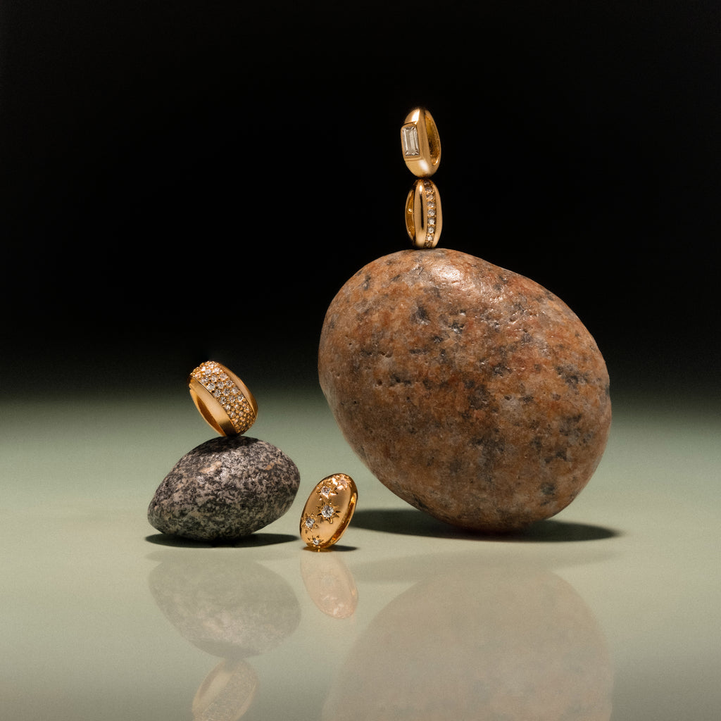 The Baguette Diamond Charm glistens elegantly atop and beside smooth stones, creating a striking display against a minimalist gradient background.