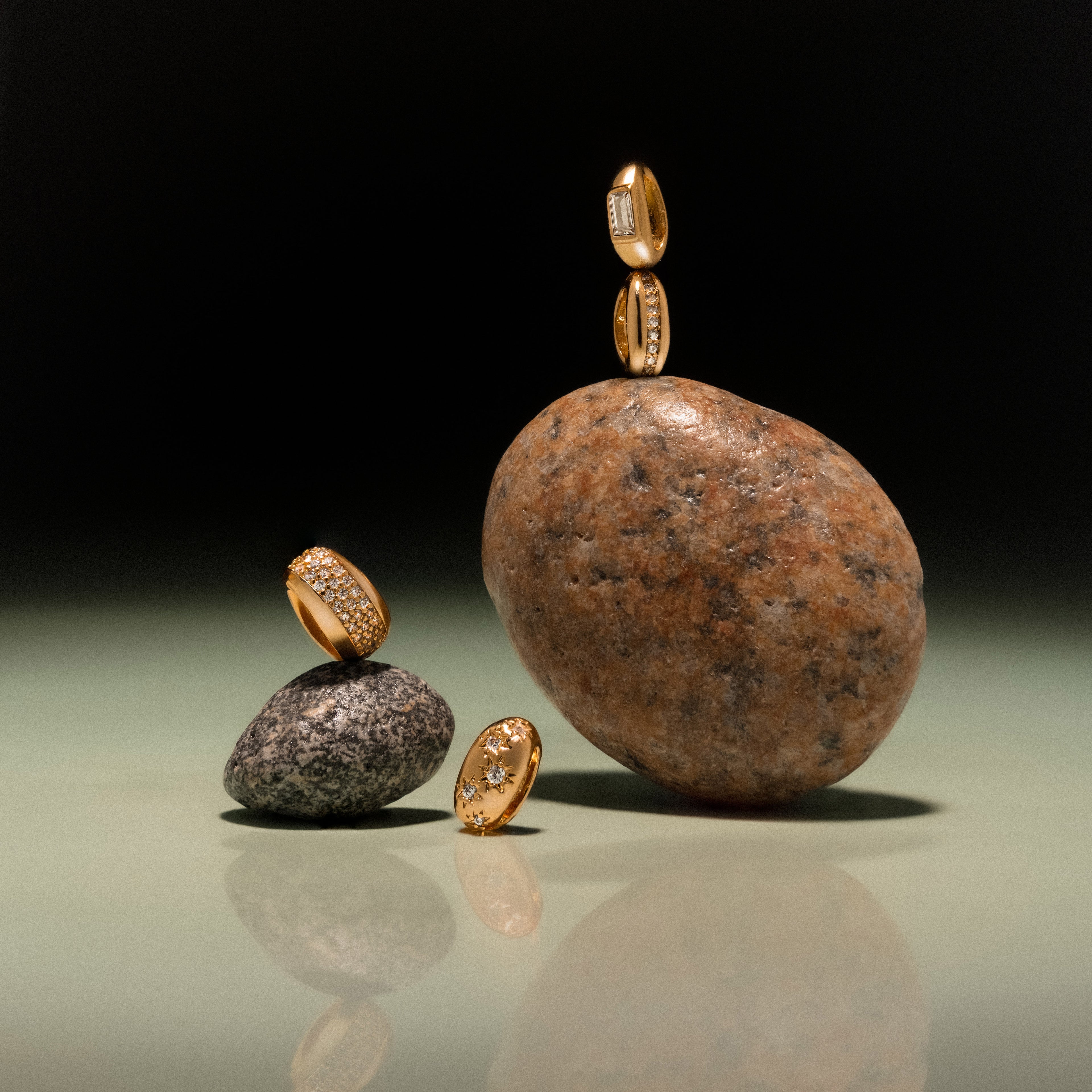 The Baguette Diamond Charm glistens elegantly atop and beside smooth stones, creating a striking display against a minimalist gradient background.
