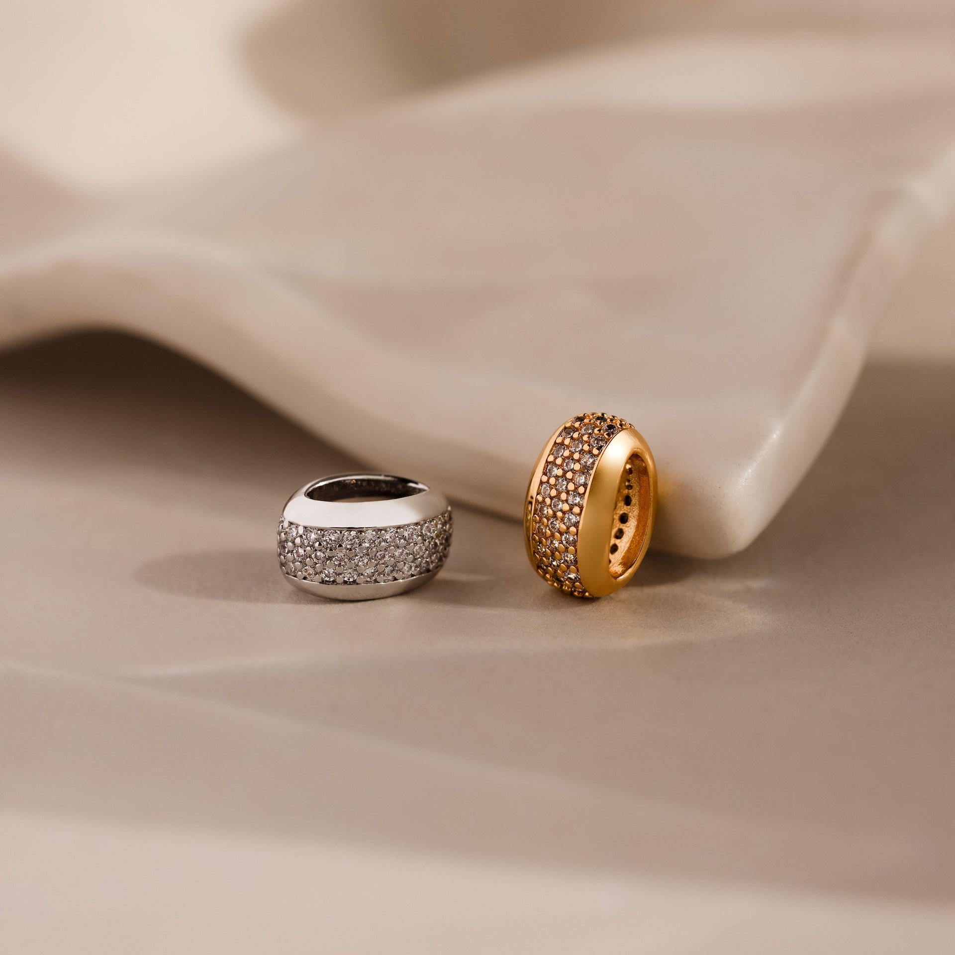 The Bold Pave Dome Charm in Silver, adorned with sparkling stones, rests elegantly on a smooth beige surface, radiating timeless charm.