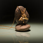 The Angel Wing Charm pendant necklace with pavé diamonds rests on two stacked brown stones atop a reflective surface—a stunning piece of protection jewelry.