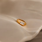 The Baguette Diamond Charm in 18K Gold shines with timeless elegance as it rests on a softly textured beige surface—an ideal choice for anyone seeking a refined and classic jewelry piece.