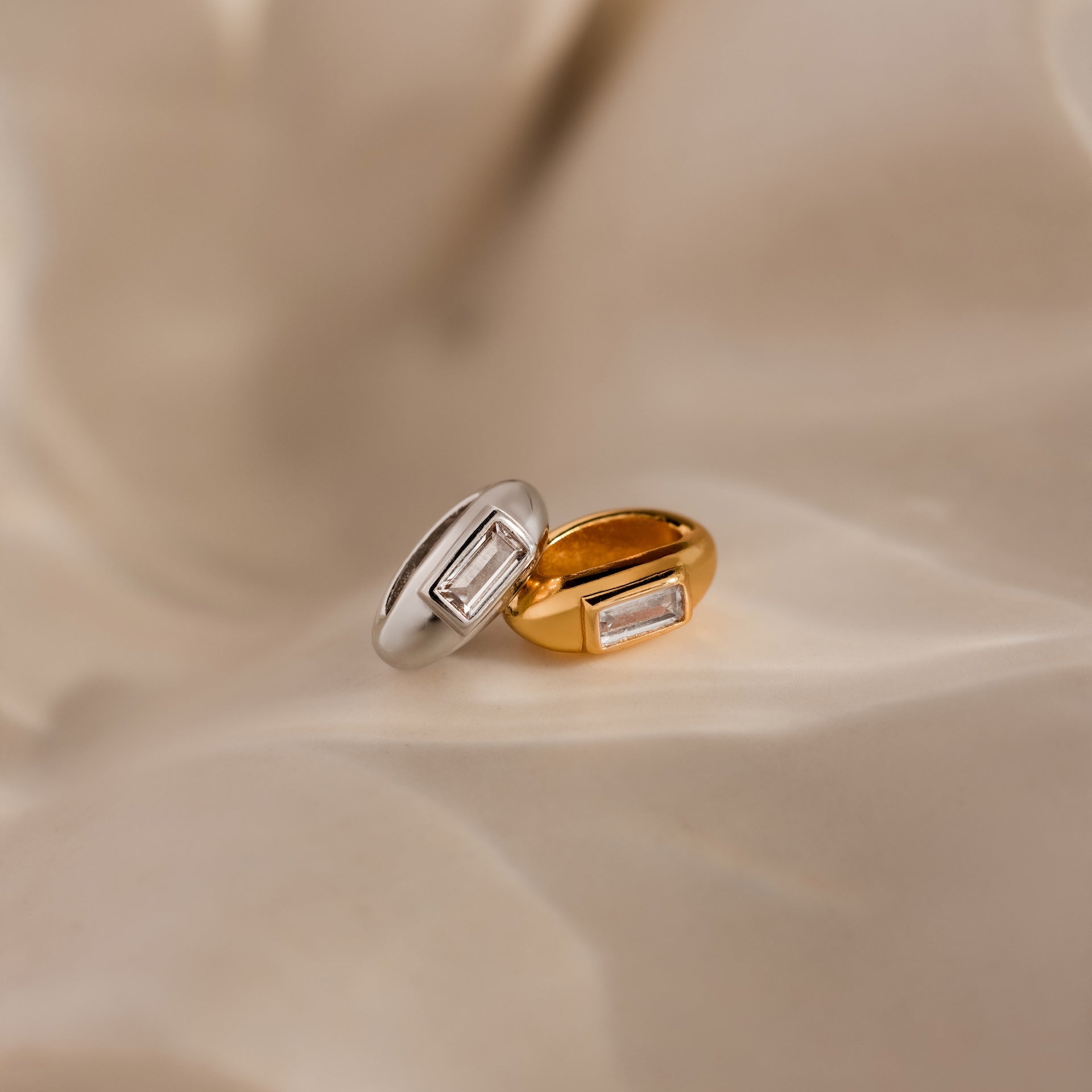 The Baguette Diamond Charm in Silver is beautifully displayed on soft beige fabric—a sophisticated addition to your jewelry collection.