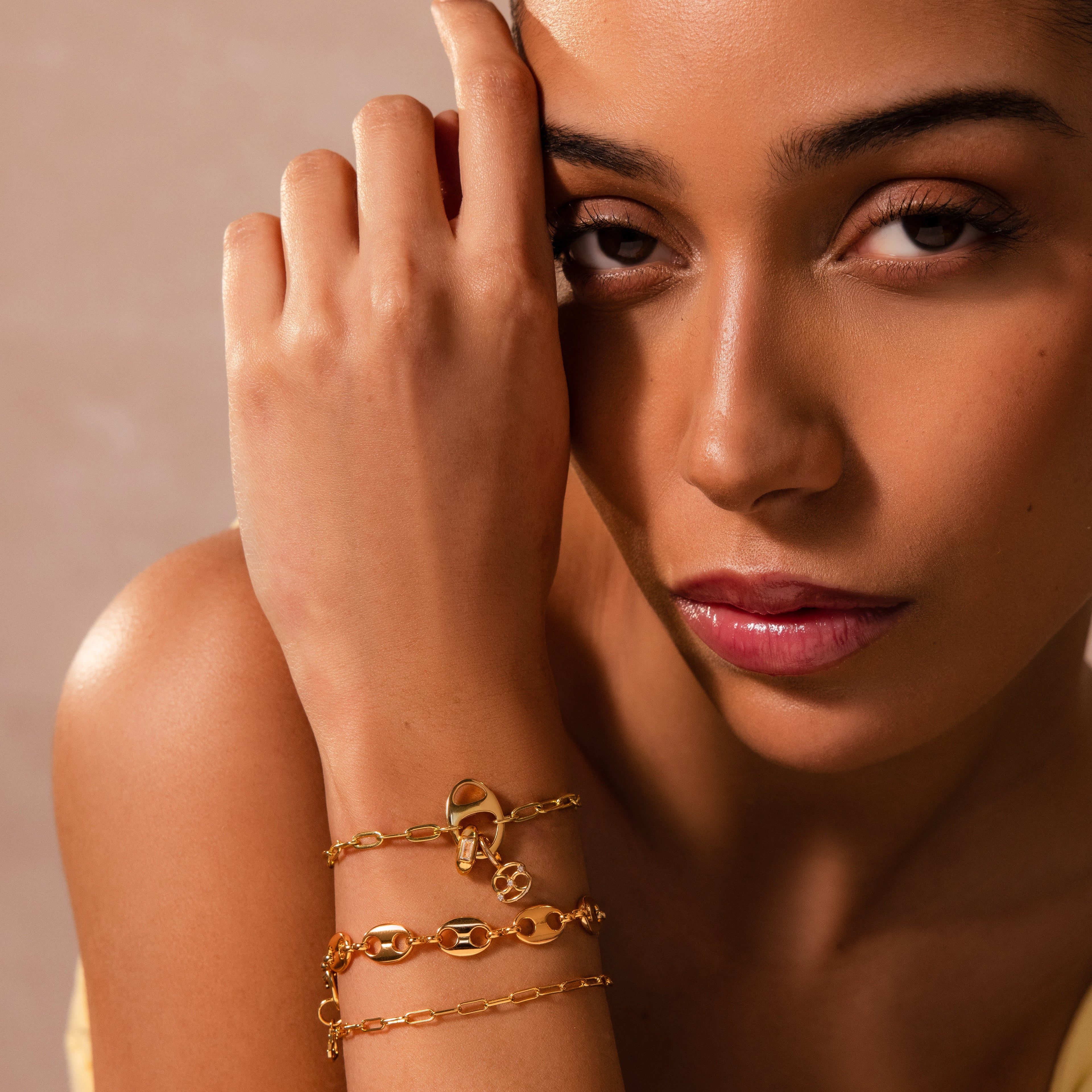 Woman gazing at camera with a Baguette Diamond Charm bracelet on her wrist, hand resting near face against a soft neutral background.