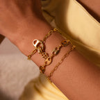 The Baguette Diamond Charm in 18K Gold shines on a wrist beside yellow fabric, its elegant design and craftsmanship making it an ideal accessory to add sophistication to any outfit.