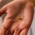 A close-up of a hand holding the Baguette Diamond Charm in 18K Gold.