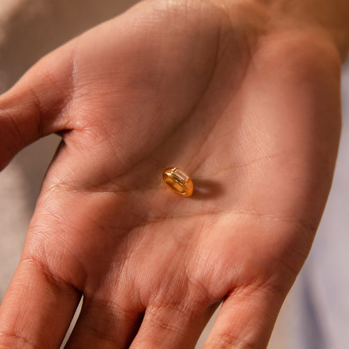 A close-up of a hand holding the Baguette Diamond Charm in 18K Gold.