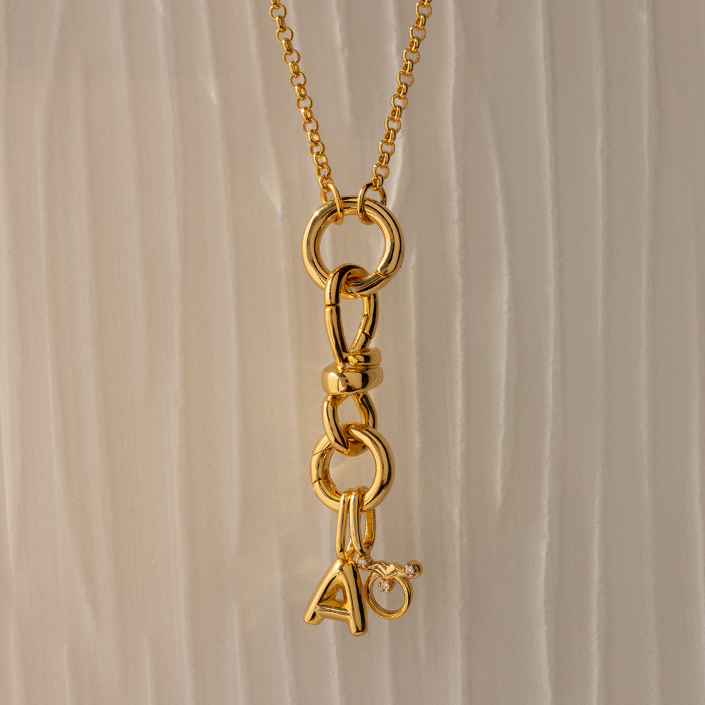 The Knot Charm Clasp in 18K Gold features interlocking links and a dangling letter A charm accented with a clear gemstone—an elegant, personalized jewelry piece ideal for gifts or everyday wear.