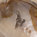 The Knot Charm Clasp is a silver keychain featuring fish, starfish, and shell charms nestled in an iridescent seashell with pearls—an ideal accessory for ocean lovers.
