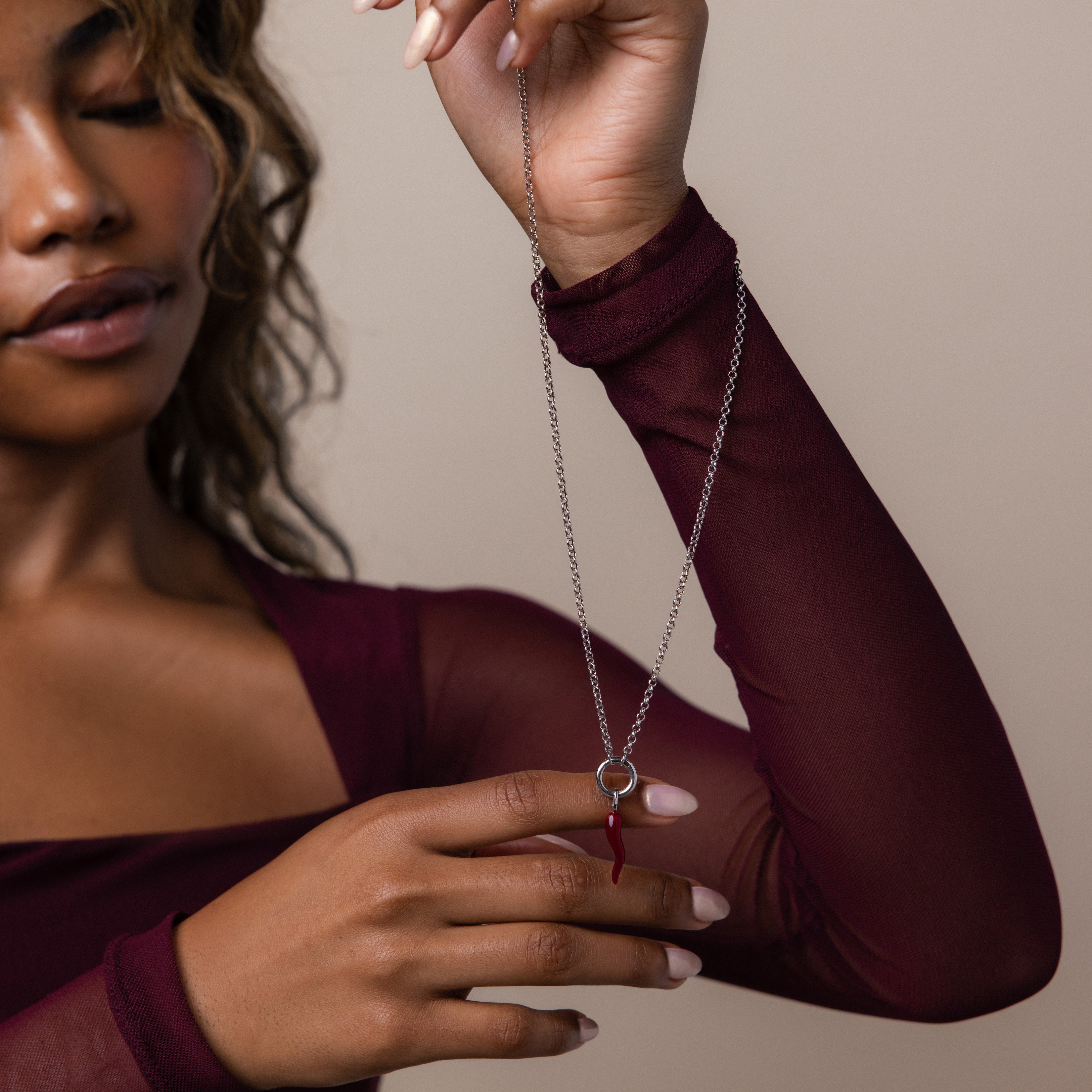 A woman in a burgundy top displays the Chili Pepper Charm necklace—a silver chain featuring a vibrant red pepper pendant—against a neutral background.