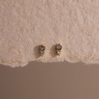 Tiny Duo Aquamarine Flatback Studs with blue and clear stones, a subtle diamond accent, displayed on textured beige paper.