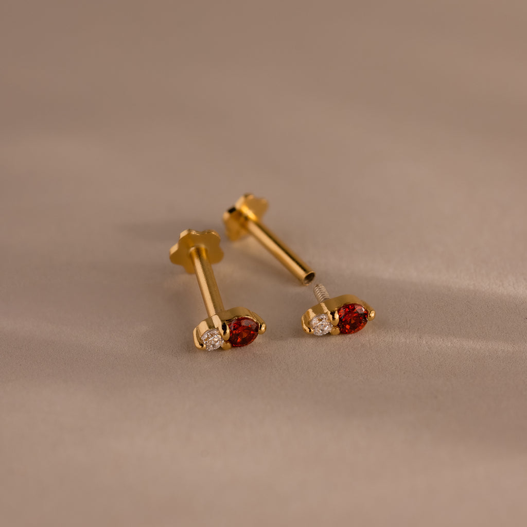 A pair of Tiny Duo Blue Zircon Flatback Studs with blue zircon stones and subtle diamond accents, ideal for an elegant ear stack, displayed on a beige surface.