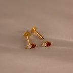 A pair of Tiny Duo Blue Zircon Flatback Studs with blue zircon stones and subtle diamond accents, ideal for an elegant ear stack, displayed on a beige surface.