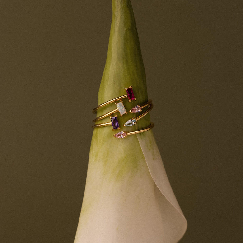 The Toi et Moi Wrap Ring in 18K Gold is displayed atop the tip of a white calla lily set against a brown background.
