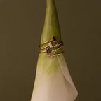 The Toi et Moi Wrap Ring in 18K Gold is displayed atop the tip of a white calla lily set against a brown background.