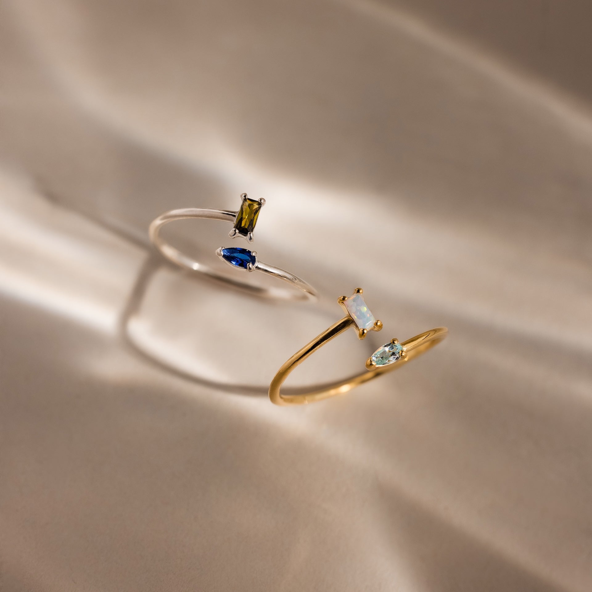 The Toi et Moi Wrap Ring features two delicate stacking rings—one silver, one gold—with colorful gemstones, elegantly displayed on a soft, neutral background.