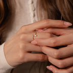 A close-up of hands with pale pink nails wearing the Toi et Moi Wrap Ring in 18K Gold, adorned with a small rectangular gemstone.