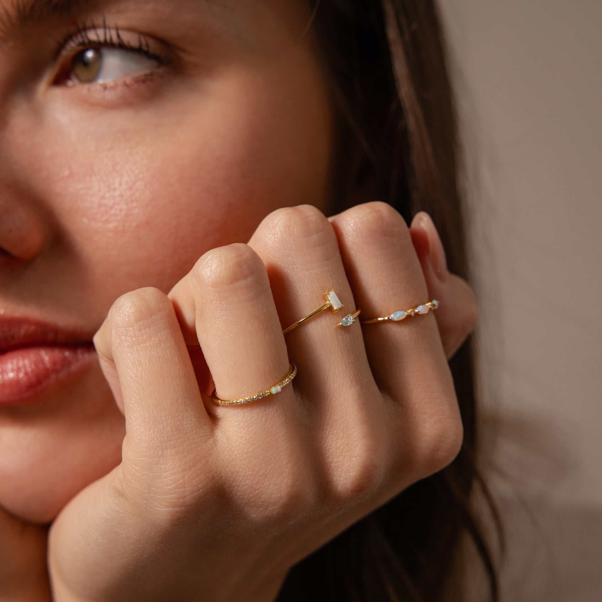 A woman’s face and hand showcasing the Toi et Moi Wrap Ring in 18K gold—a delicate ring with small gemstones, perfect for stacking.