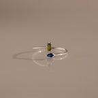 The Toi et Moi Wrap Ring features a rectangular yellow gemstone and a marquise blue gemstone set in silver, displayed on a neutral background—a timeless romantic jewelry piece.