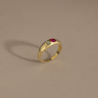The Toi et Moi Dome Ring in 18K Gold features a rectangular green stone and a round red stone set side by side, displayed on a beige background.
