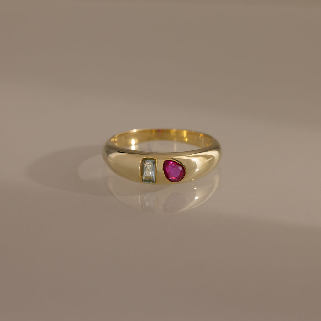 The Toi et Moi Dome Ring features a rectangular clear stone and a round red stone set side by side, creating a bold birthstone-inspired look.
